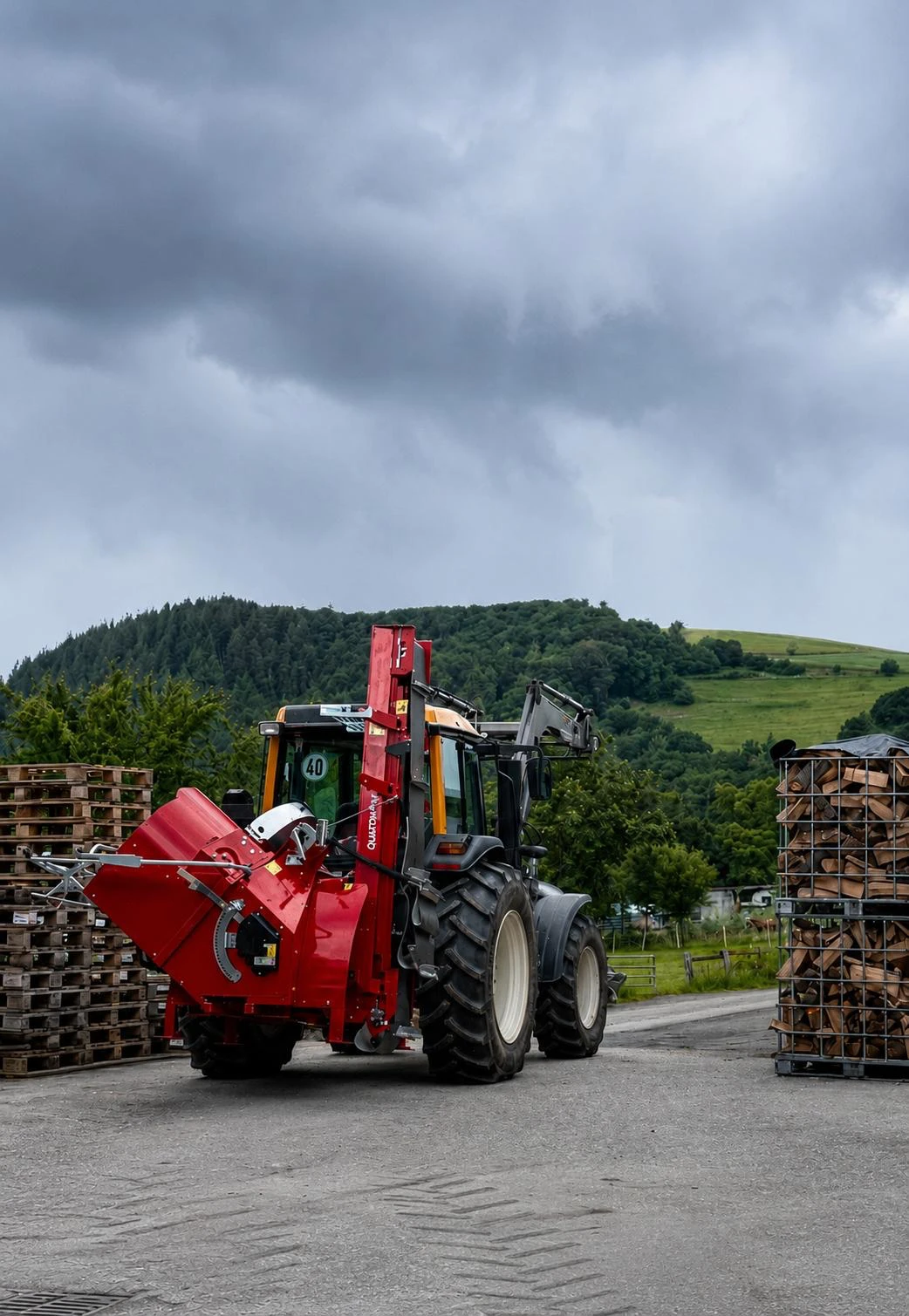 Roter Sägespaltautomat am Traktor, im Hintergrund eine Gitterbox mit Brennholz